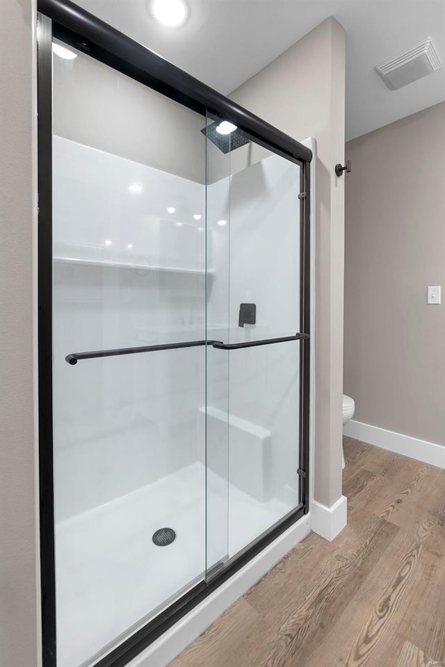 bathroom with toilet, an enclosed shower, and hardwood / wood-style floors