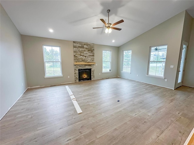 unfurnished living room with ceiling fan, a stone fireplace, vaulted ceiling, and light wood-type flooring