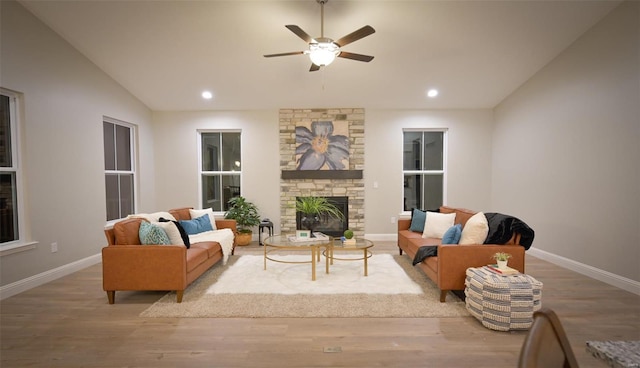 living room with a stone fireplace, wood-type flooring, ceiling fan, and vaulted ceiling