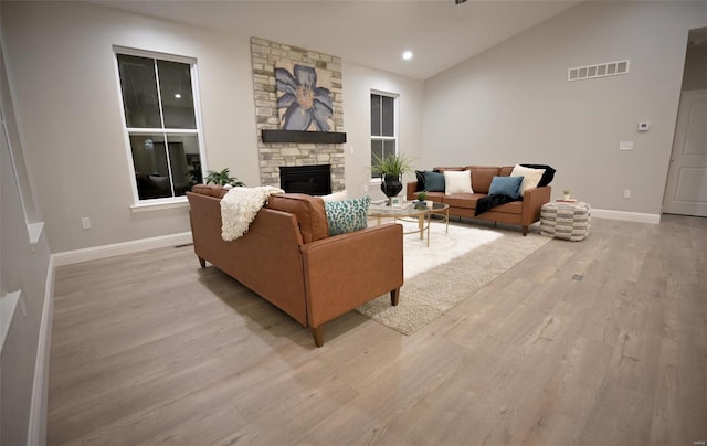 living room with a fireplace, vaulted ceiling, and light wood-type flooring