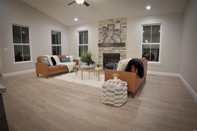 living room featuring lofted ceiling, a fireplace, ceiling fan, and light wood-type flooring