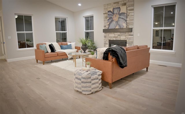 living room with lofted ceiling, a stone fireplace, and light wood-type flooring