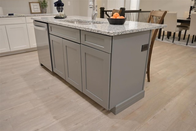 kitchen featuring light stone counters, light hardwood / wood-style flooring, stainless steel dishwasher, gray cabinets, and an island with sink