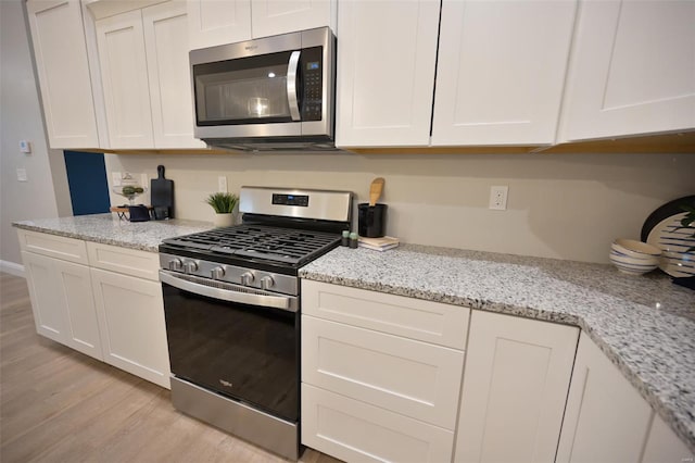 kitchen featuring white cabinetry, appliances with stainless steel finishes, light stone counters, and light hardwood / wood-style flooring