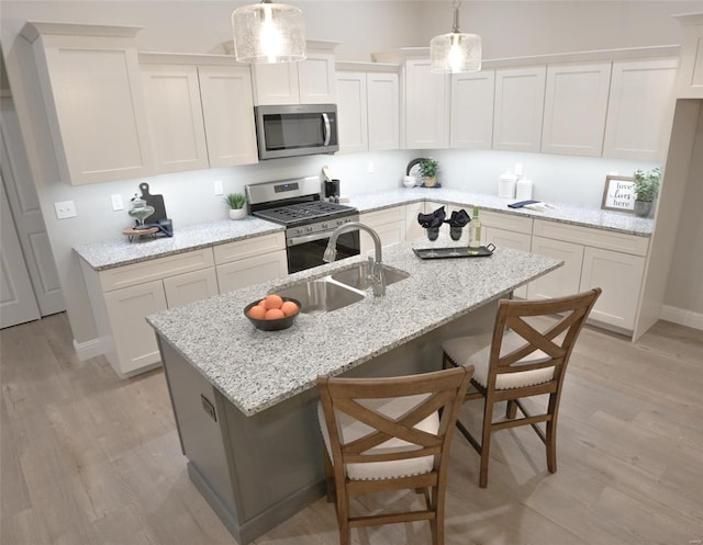 kitchen featuring hanging light fixtures, a kitchen island with sink, stainless steel appliances, light stone countertops, and light wood-type flooring