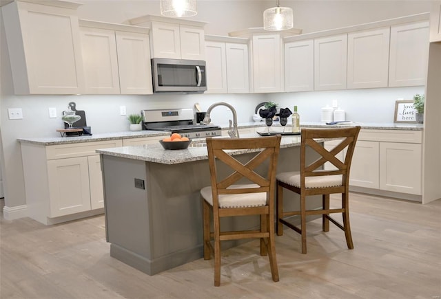 kitchen with a kitchen island with sink, hanging light fixtures, light wood-type flooring, and appliances with stainless steel finishes