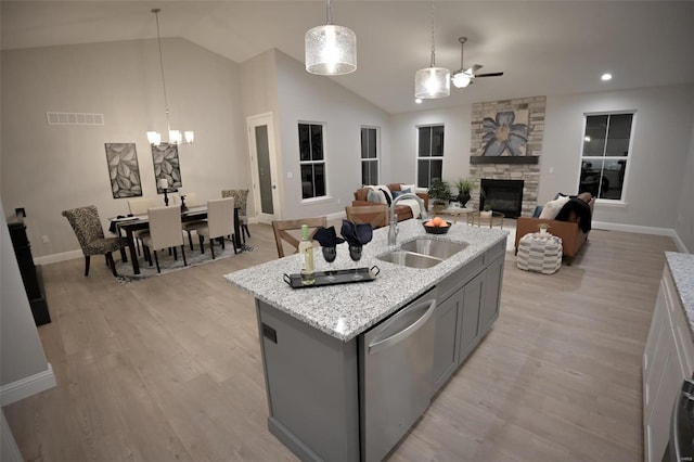 kitchen featuring sink, dishwasher, hanging light fixtures, a fireplace, and an island with sink