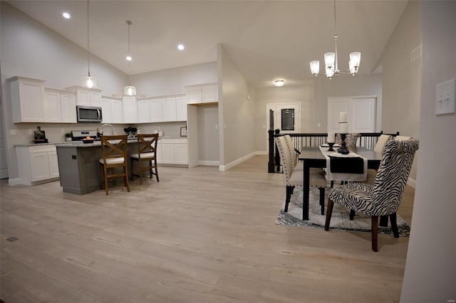 dining area with an inviting chandelier, high vaulted ceiling, and light hardwood / wood-style flooring