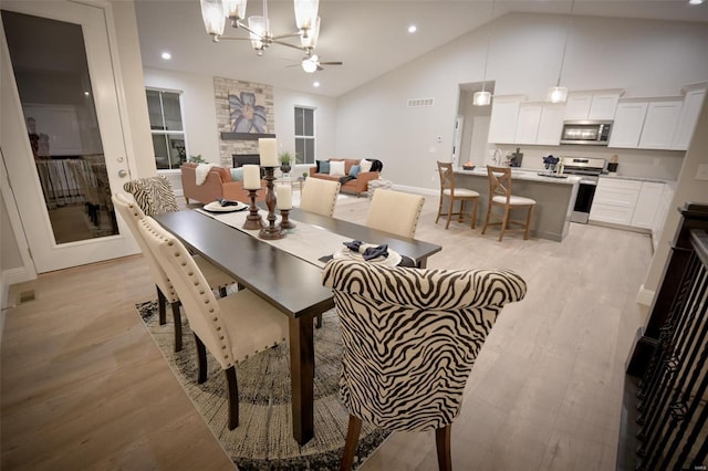 dining space featuring ceiling fan with notable chandelier, lofted ceiling, a stone fireplace, and light hardwood / wood-style floors