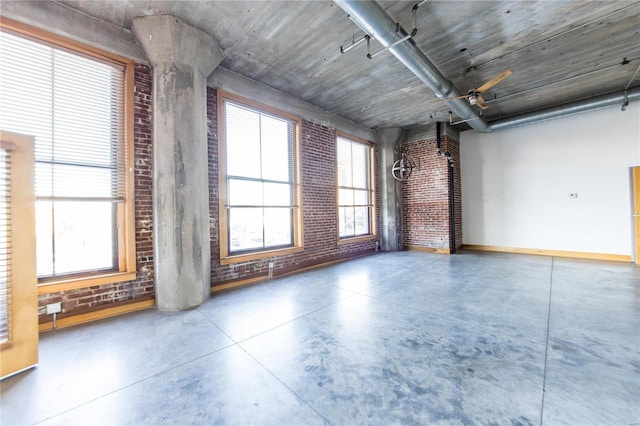 empty room featuring plenty of natural light, ceiling fan, concrete flooring, and brick wall