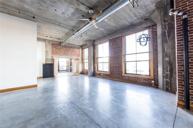 unfurnished living room with ceiling fan, concrete flooring, and brick wall