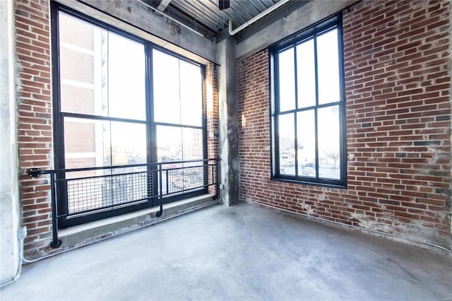 empty room with a wealth of natural light, concrete flooring, and brick wall