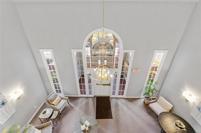 living area featuring a healthy amount of sunlight, a towering ceiling, carpet floors, and a notable chandelier