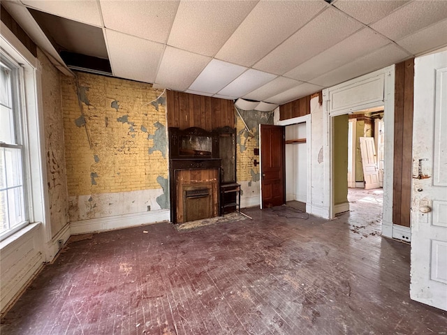 unfurnished living room with a paneled ceiling and brick wall