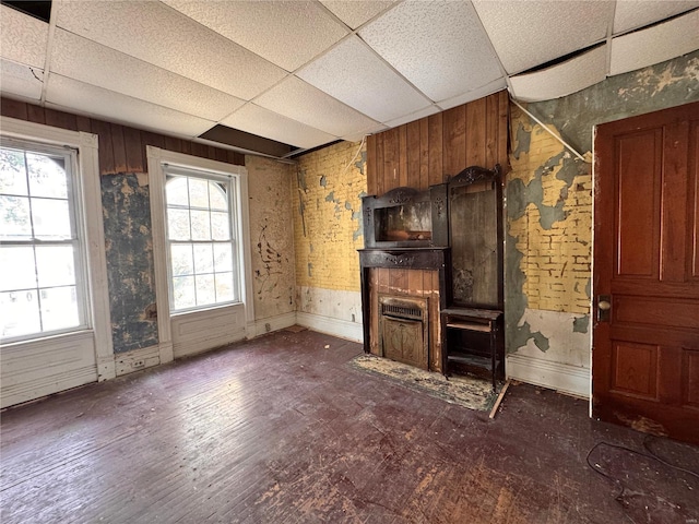 unfurnished living room featuring a drop ceiling, dark hardwood / wood-style floors, and wood walls