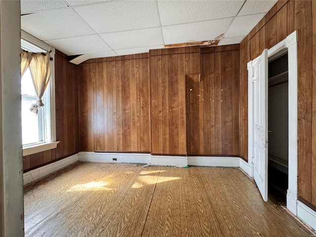 spare room with a paneled ceiling, hardwood / wood-style flooring, and wood walls