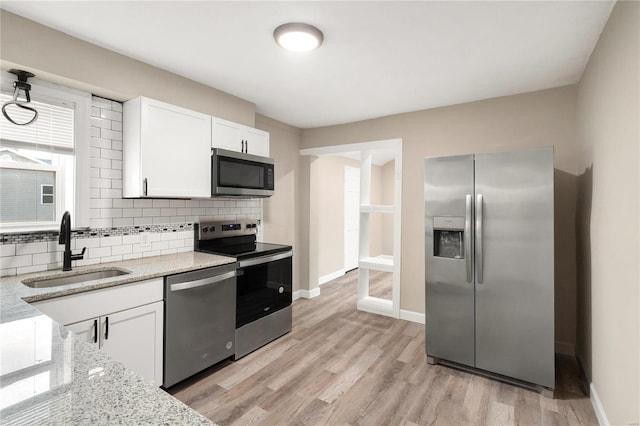 kitchen with light hardwood / wood-style floors, white cabinetry, sink, appliances with stainless steel finishes, and light stone countertops