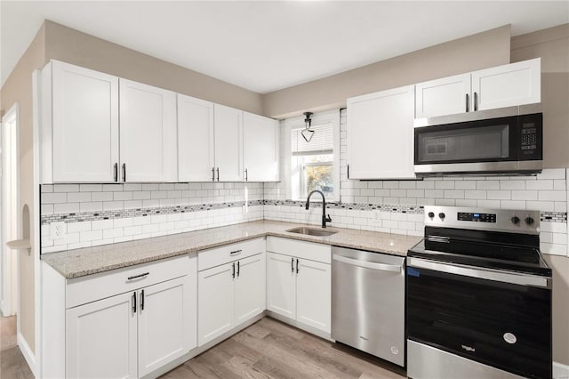 kitchen with tasteful backsplash, stainless steel appliances, sink, white cabinets, and light hardwood / wood-style flooring