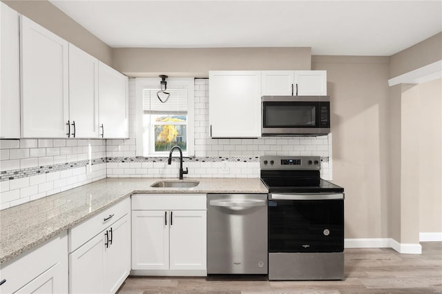 kitchen featuring sink, light stone countertops, white cabinetry, light wood-type flooring, and appliances with stainless steel finishes