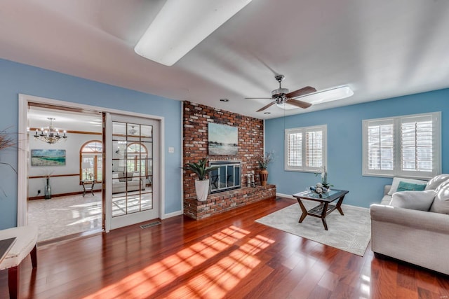 living room featuring a brick fireplace, ceiling fan with notable chandelier, and wood-type flooring