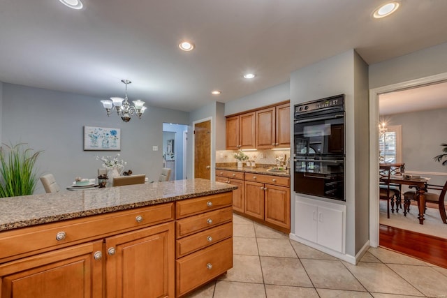 kitchen featuring light stone counters, a chandelier, light tile patterned floors, black double oven, and pendant lighting