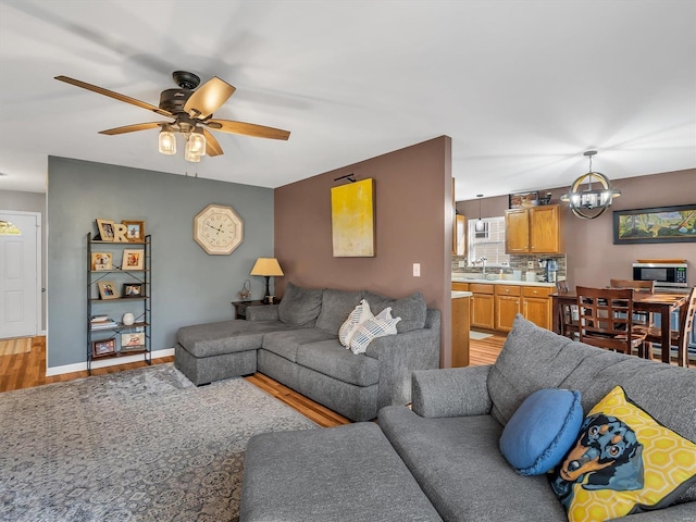 living area with light wood-style flooring, ceiling fan with notable chandelier, and baseboards