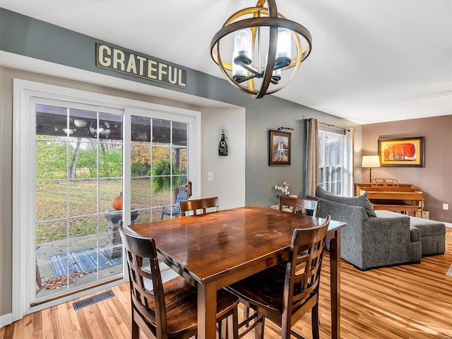 dining space with baseboards, light wood-style floors, an inviting chandelier, and visible vents