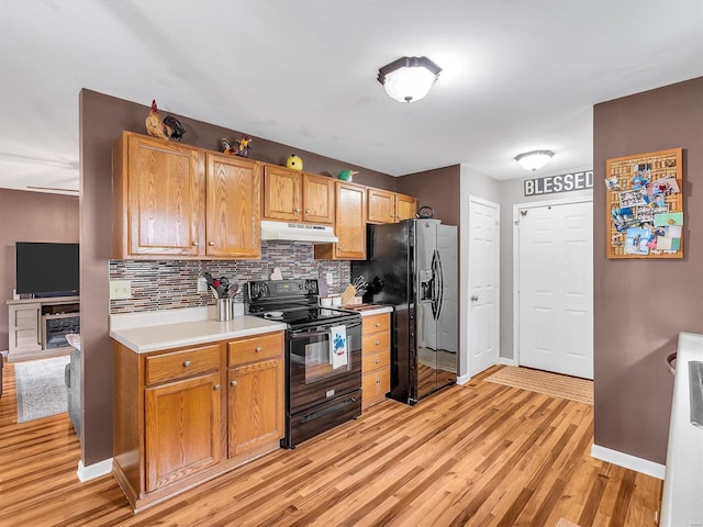 kitchen featuring under cabinet range hood, baseboards, decorative backsplash, black appliances, and light wood-type flooring