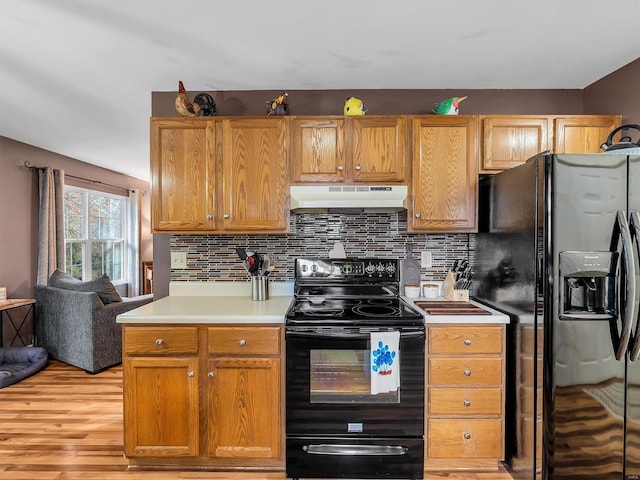 kitchen featuring black appliances, under cabinet range hood, light wood finished floors, decorative backsplash, and light countertops