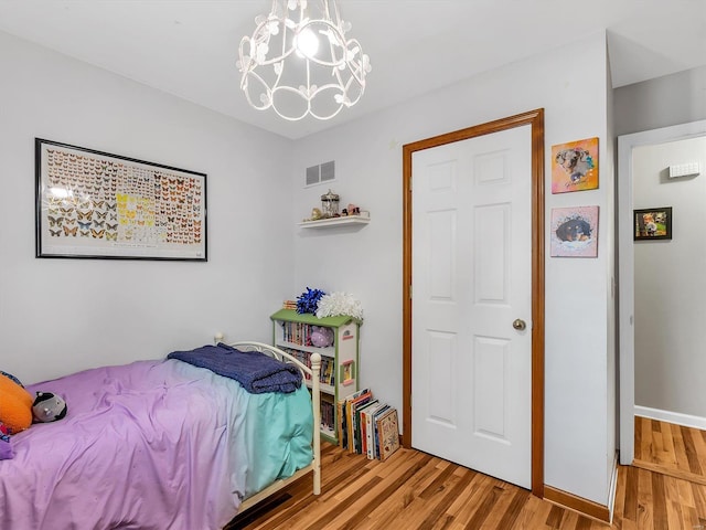 bedroom featuring visible vents, wood finished floors, baseboards, and a notable chandelier