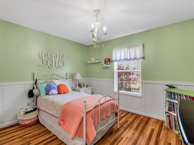 bedroom with wainscoting, an inviting chandelier, and wood finished floors