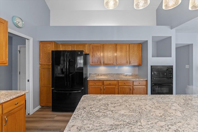 kitchen featuring light stone counters, black appliances, and light hardwood / wood-style floors