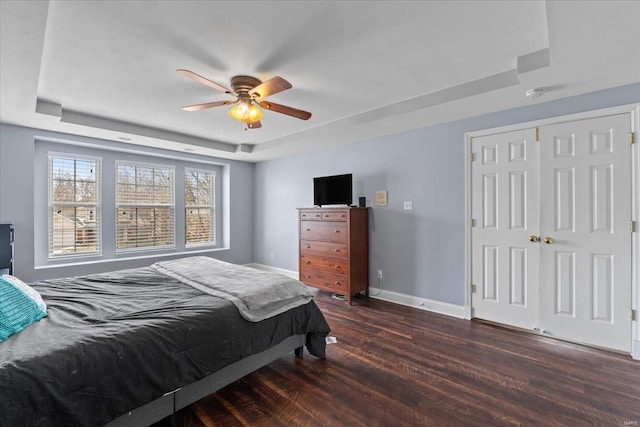 bedroom featuring a closet, dark wood-type flooring, a raised ceiling, and ceiling fan