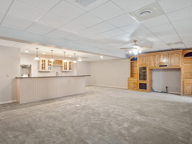 unfurnished living room with light colored carpet, wet bar, a drop ceiling, and ceiling fan