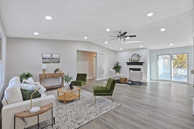 living room with ceiling fan, light hardwood / wood-style floors, a fireplace, and vaulted ceiling