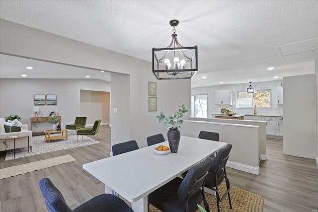 dining area featuring sink, light wood-type flooring, a textured ceiling, and a notable chandelier