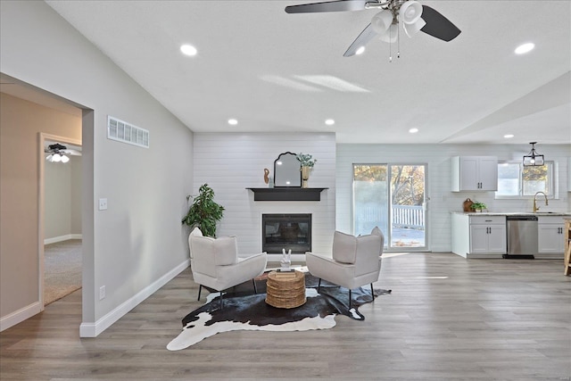 living room featuring ceiling fan, a fireplace, light hardwood / wood-style floors, and lofted ceiling