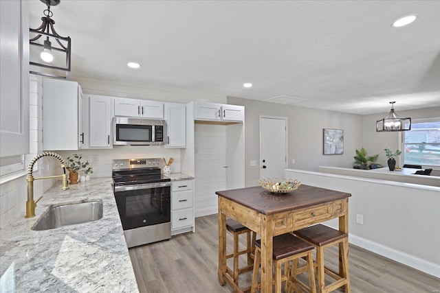 kitchen featuring light stone counters, stainless steel appliances, sink, pendant lighting, and white cabinetry