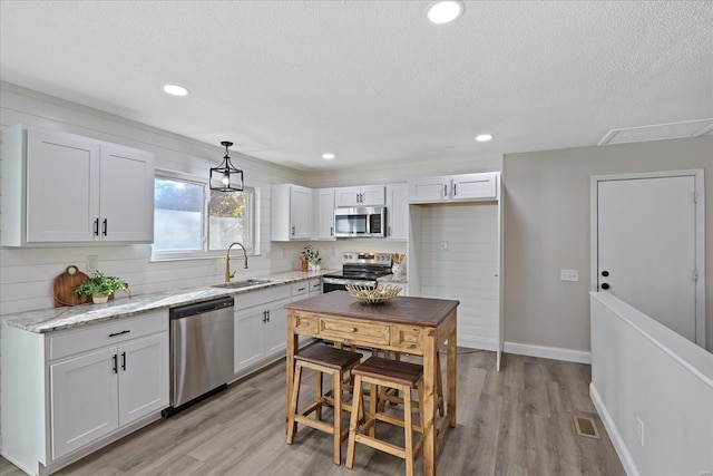 kitchen with appliances with stainless steel finishes, white cabinetry, hanging light fixtures, and sink