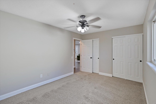 unfurnished bedroom with ceiling fan, light carpet, and two closets