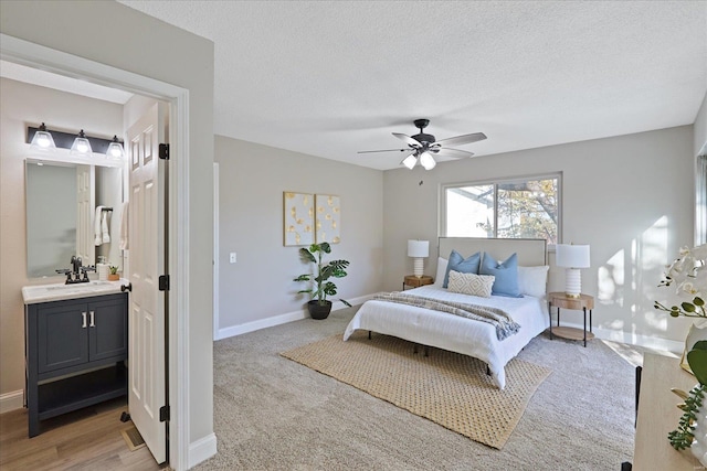 carpeted bedroom featuring a textured ceiling, ensuite bathroom, ceiling fan, and sink