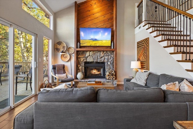 living room with a stone fireplace, high vaulted ceiling, and wood-type flooring