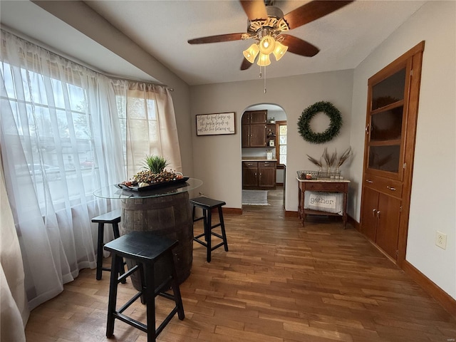 dining space with baseboards, arched walkways, dark wood finished floors, and a ceiling fan