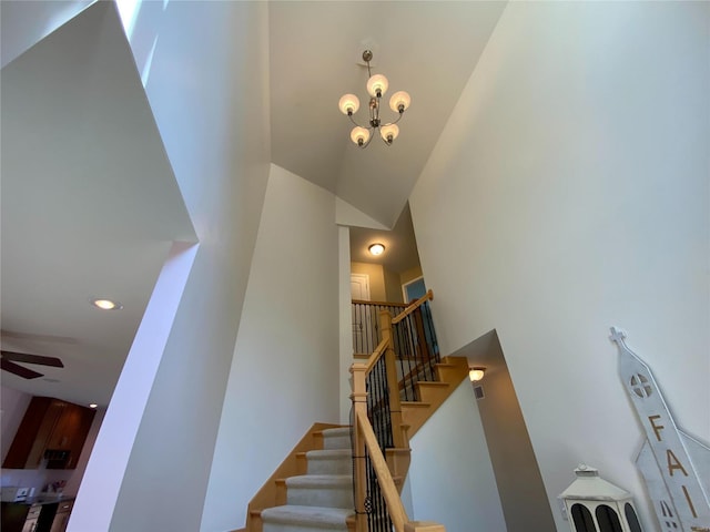 staircase featuring high vaulted ceiling and ceiling fan with notable chandelier