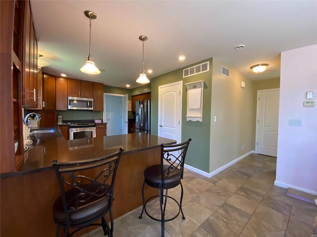 kitchen with appliances with stainless steel finishes, sink, a kitchen bar, kitchen peninsula, and hanging light fixtures