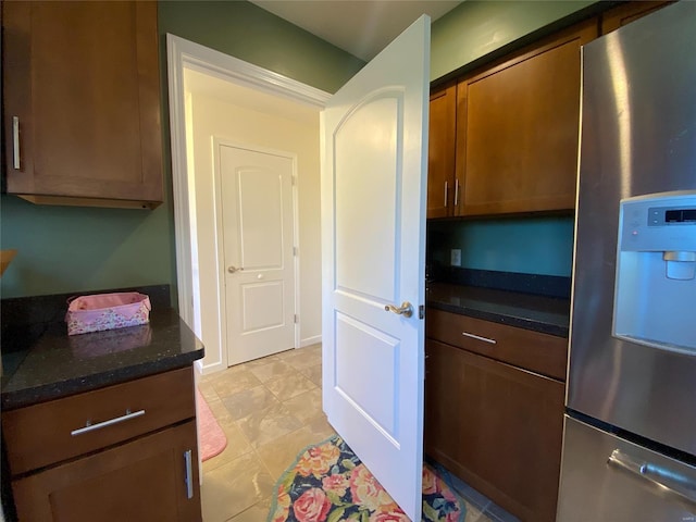 kitchen featuring dark stone countertops, light tile patterned flooring, and stainless steel fridge