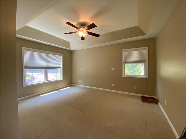 carpeted spare room with a wealth of natural light, ceiling fan, and a raised ceiling