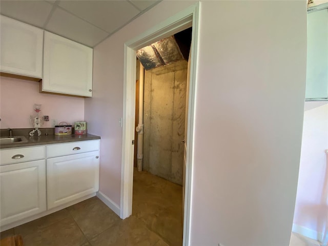 kitchen featuring sink, light tile patterned floors, a drop ceiling, and white cabinets