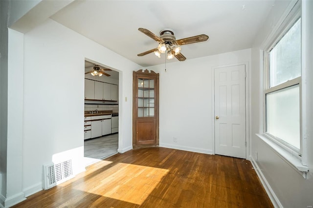 empty room with visible vents, a ceiling fan, plenty of natural light, and wood finished floors