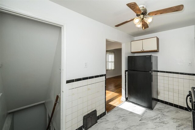 kitchen featuring freestanding refrigerator, a ceiling fan, a wainscoted wall, and tile walls